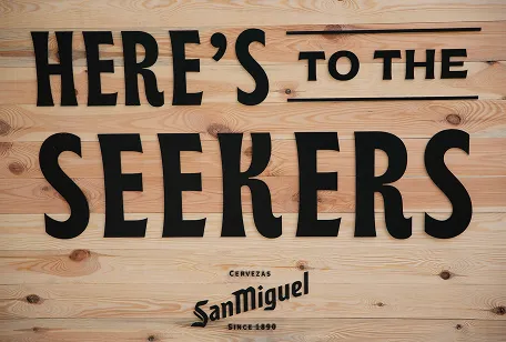 Wooden panel with San Miguel logo and the phrase “Here’s to the Seekers”.