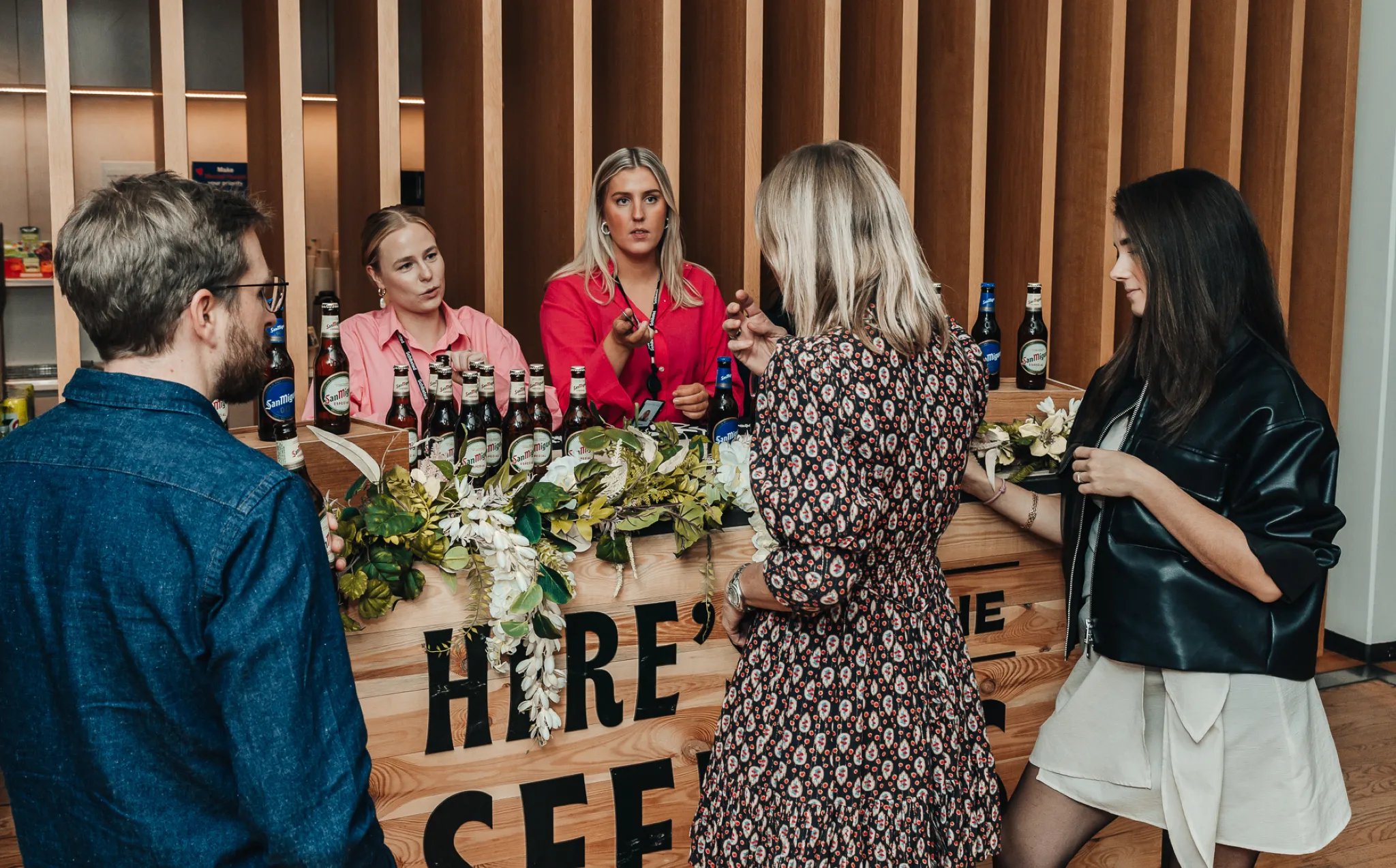 People interacting at a San Miguel beer tasting counter during an indoor event.