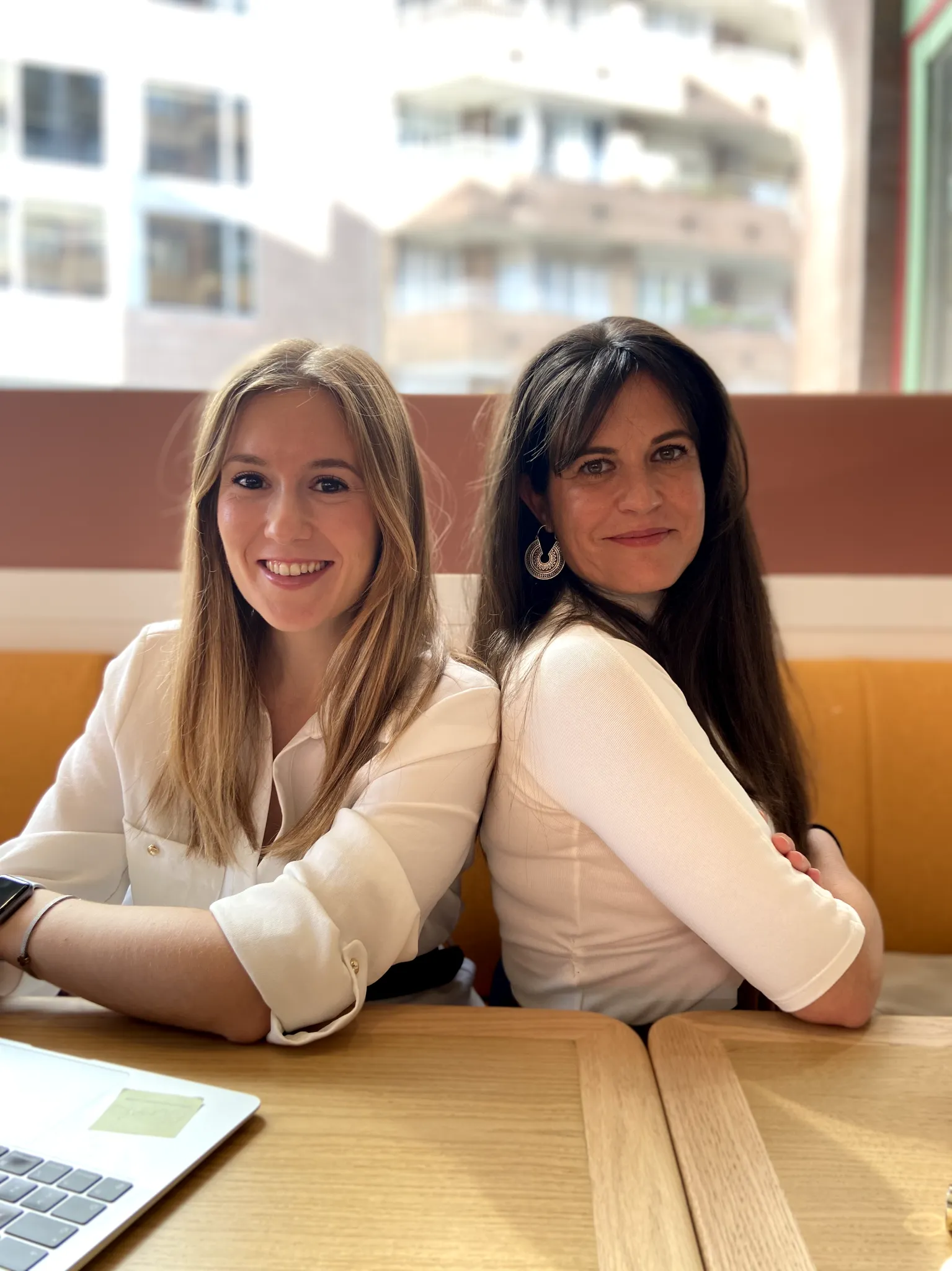 The founders of Atlas Marketing Studio sitting back-to-back at a wooden table, smiling confidently in a bright, modern office setting.
